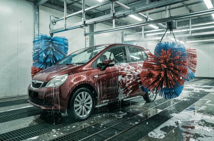 Voiture rouge traversant un tunnel de lavage automatique professionnel avec brosses rotatives et jets d'eau, dans une station de lavage près de Metz